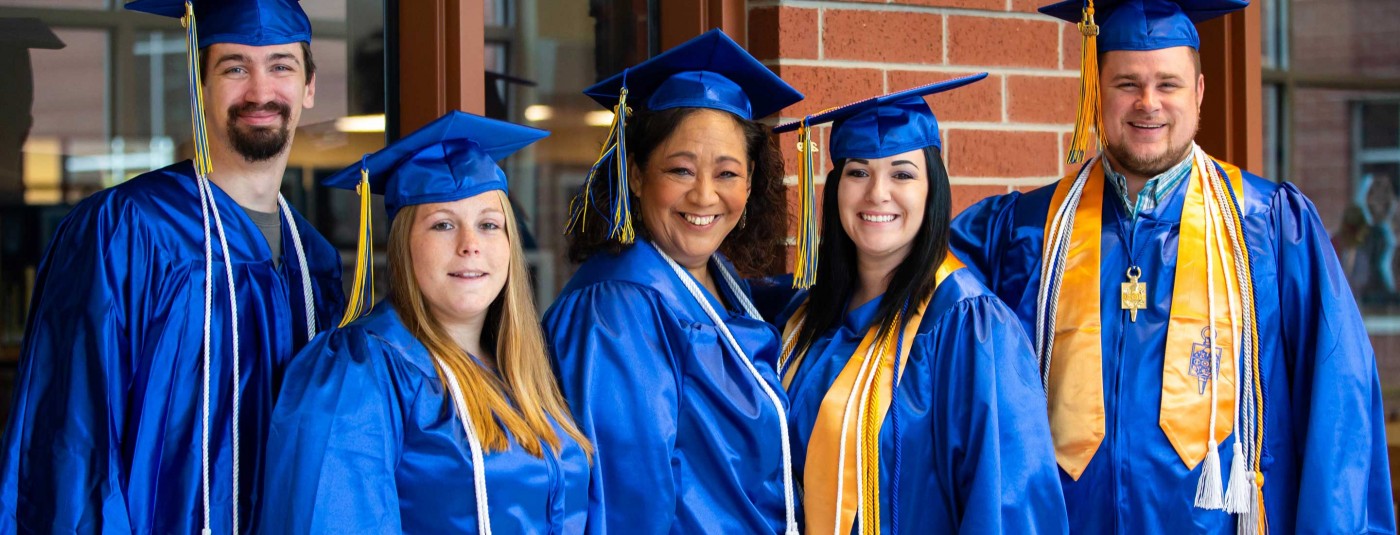 Five graduates in cap and gowns smiling together