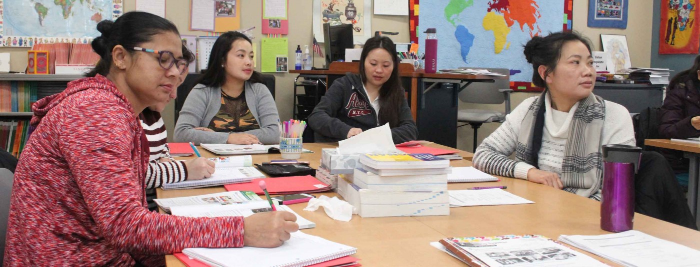 Five students sitting together at classroom table taking class notes