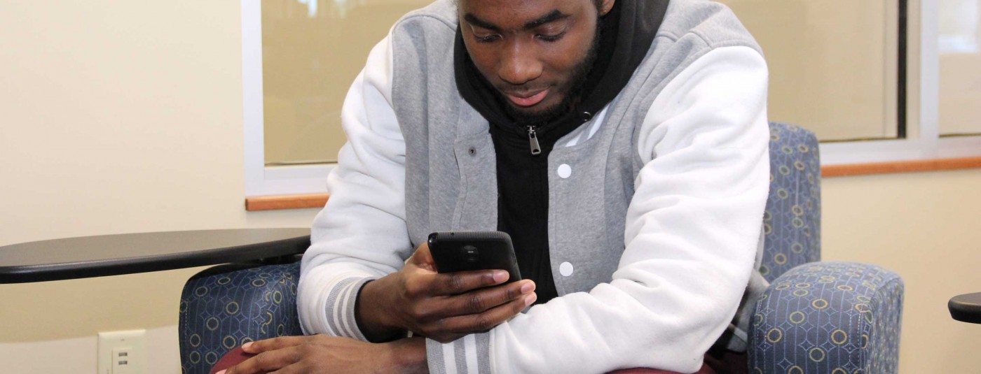 Student in campus waiting room looking at mobile phone